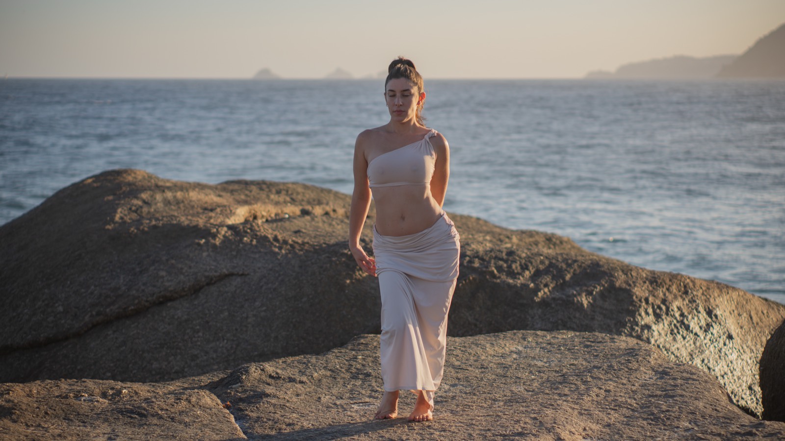 Gabriela caminhando à beira do mar ao entardecer